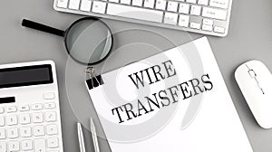 WIRE TRANSFERS written on paper with office tools and keyboard on the grey background