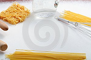 Wire whisk, macaroni and rolling pin on flour
