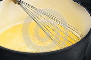 Wire whisk in a pot with golden yellow semolina flummery or pudding, cooking a delicious dessert, copy space, selected focus