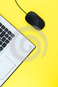 The wired computer mouse and the laptop are isolated on a yellow background. Flat lay template for design.