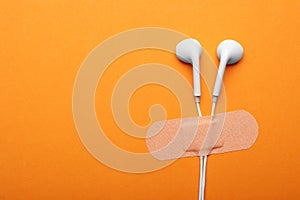 Wired earphones with sticking plaster on orange background, flat lay. Space for text