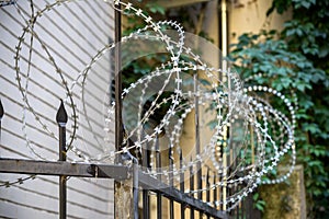 Wired fence with rolled barbed wires with house from brick wall on background. Protection and safety concept