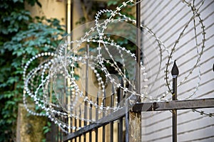 Wired fence with rolled barbed wires with house from brick wall on background. Protection and safety concept