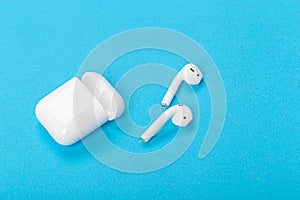 Wireless bluetooth earphones with charging case on a blue background. The concept of modern technology
