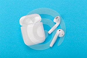 Wireless bluetooth earphones with charging case on a blue background. The concept of modern technology