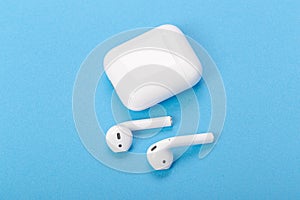 Wireless bluetooth earphones with charging case on a blue background. The concept of modern technology