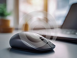 Wireless computer mouse placed on a desk surface with a blurred laptop and warm natural light streaming through a window in the