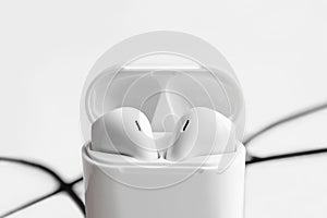 Wireless ear buds in glossy white plastic case on white background