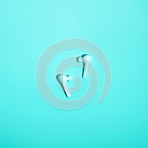 Wireless in ear headphones on blue background close up. Minimal music concept. White earphones flat lay, top view