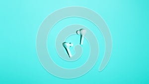 Wireless in ear headphones on blue background close up. Minimal music concept. White earphones flat lay, top view