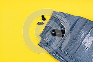 wireless earbuds, jeans and charging case on yellow background