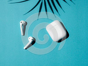 Wireless headphones on blue background with palm leaves shadow