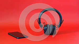 Wireless headphones with ear pads next to a smartphone on a red background. The concept of listening to music, radio and audio