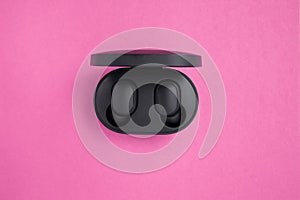 Wireless headphones in a mockup case on a bright pink background with text space. Black earphones in a case with charg