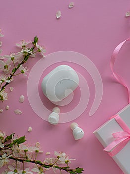 Wireless headphones on pink background with cherry flowers and copy space