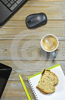 Wireless mouse, optical, cup of coffee, piece of bread and a notebook with pen on a wooden surface
