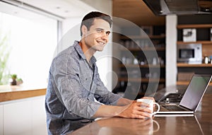 Wireless thinking. a young man contemplating while sitting at his kitchen table with his laptop.