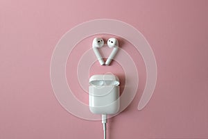 Wireless white headphones on pink background. Airpods. wireless white headphones with charger connected. Copy space photo