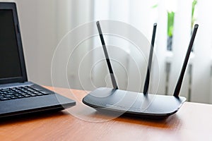 wireless wifi router and laptop at wooden table indoors. window behind. wireless connection concept