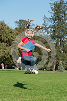 The wise choice for audio fanatics. Happy child jump on green grass. Small girl listen to audio book playing in