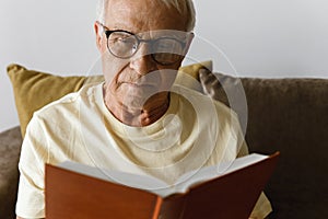 Wise and elderly man is reading book at home