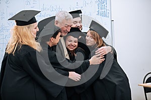 A wise elderly university professor rejoices together with his students in robes and hats at the end of their studies