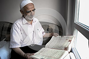Wise old muslim man wearing taqiyah reads Turkish translation of Quran in passion