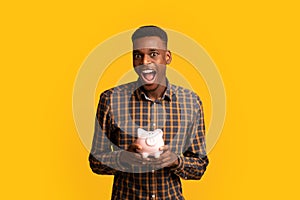 Wise Saving. Portraif Of Funny Excited Black Guy Holding Piggy Bank