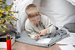 A wish list for a Christmas miracle. A little cute boy draws a dream gift from Santa Claus at home.