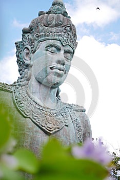 Wisnu statue on clear weather with bird is flying above it photo