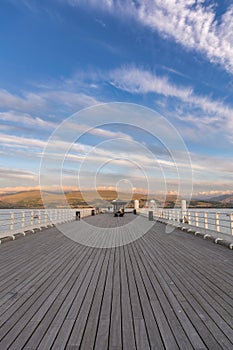 Wispy high clouds over a long wooden pier with mountains in the distance. Beaumaris, North Wales