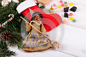 The witch Befana and red stocking with sweet coal and candy on white wooden background