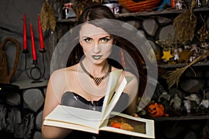 witch in a black corset with a book in his hands conjures reads a spell. Girl in costume on halloween