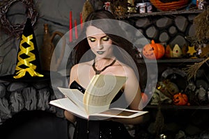 witch in a black corset with a book in his hands  conjures  reads a spell. Girl in costume on halloween