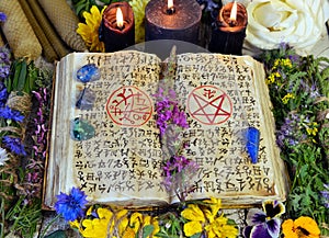 Witch book with spells and symbols, black candles, reiki crystals and flowers
