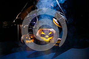 Witch casts a spell on a steaming pumpkin in the dark on Halloween
