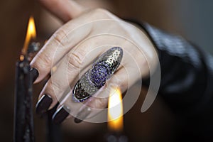 Witch`s hands with black manicure and a ring over the flame of candles. Occultism, magic and rituals. Close-up