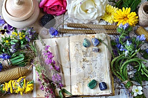 Witch spell book, calendula, rose flowers, reiki crystals and candles on wooden table