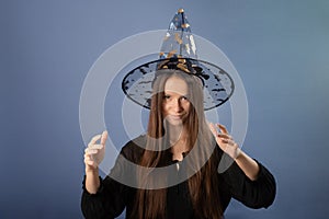 Witch teenager girl in Halloween in hat conjures on a gray background photo