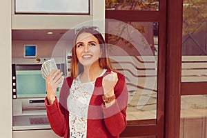 Withdraw.  ATM. Portrait happy smiling woman exults pumping fists ecstatic celebrates success holding cash dollar money bills