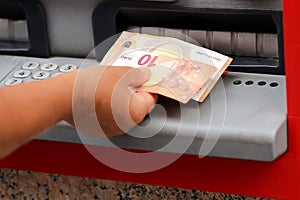 Withdrawing euros from an ATM from bank outdoors in Europe city. adult female hand holding European banknotes
