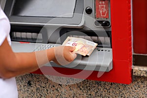 Withdrawing euros from an ATM from bank outdoors in Europe city. adult female hand holding European banknotes