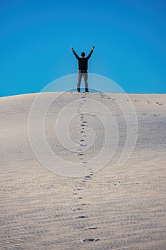 Witness the triumphant spirit of a man raising his hand in triumph with track of footprints at the top of White Sands National