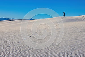 Witness the triumphant spirit of a man raising his hand in triumph with track of footprints at the top of White Sands National