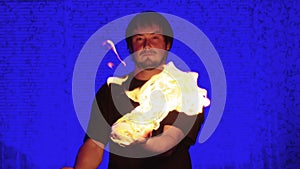 Wizard on blue background holds a burning hand in front of him. The magician shows the element of fire in the camera