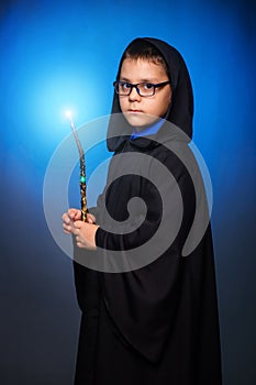 A wizard boy in glasses with a magic wand in his hands and in a black robe with a hood conjures a spell photo