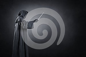 Wizard with hooded cape and magic wand over dark background