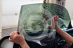 The wizard for installing additional equipment sticks a tint film on the side front glass of the car and flattens it by hand to photo