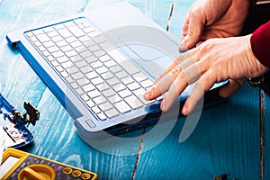 Wizard repairs laptop with tools and hands on the blue wooding table. top view