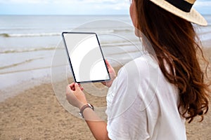 A woamn holding a black tablet pc with blank desktop screen by the sea